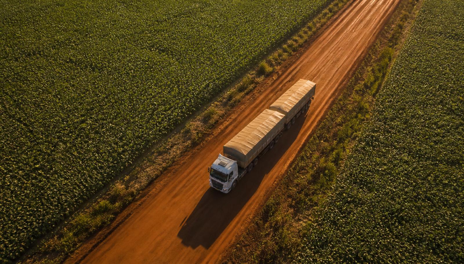 Vista aérea de carreta graneleira em estrada de terra entre lavouras